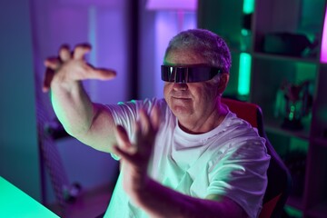 Poster - Middle age grey-haired man streamer playing video game using virtual reality glasses at gaming room