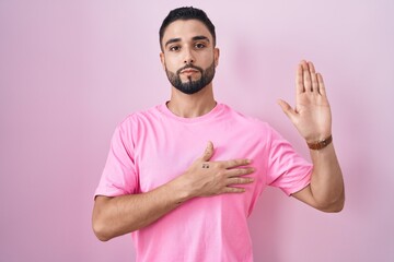 Canvas Print - Hispanic young man standing over pink background swearing with hand on chest and open palm, making a loyalty promise oath