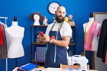 Sticker - Young bald man tailor smiling confident using smartphone at clothing factory