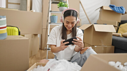 Poster - Young beautiful hispanic woman playing video game by smartphone at new home