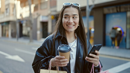 Sticker - Young beautiful hispanic woman using smartphone holding shopping bags and coffee at street