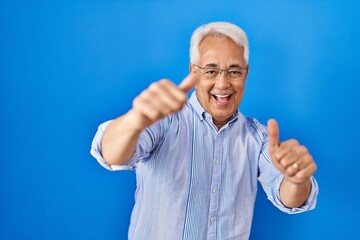 Poster - Hispanic senior man wearing glasses approving doing positive gesture with hand, thumbs up smiling and happy for success. winner gesture.