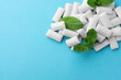 Pile of tasty white chewing gums and mint leaves on light blue background, top view. Space for text