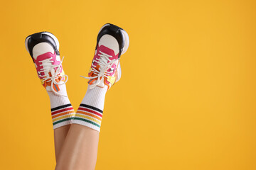 Wall Mural - Woman wearing stylish sneakers on yellow background, closeup. Space for text