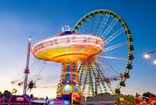 Funfair panorama wiht ferris wheel and carousels on big german funfair or Kirmes at blue hour twilight. Long time exposure with multi color light traces.
