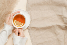 Female Hands Hold Cup Of Tea With Lemon On Linen Beige Cloth Background, Copy Space. Woman With Cup Of Tea, Cozy Atmosphere, Aesthetic Minimal Style. Autumn And Winter Theme