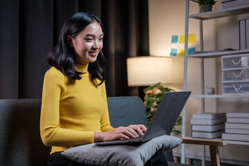 Poster - Happy asian woman sitting on sofa in living room, using laptop