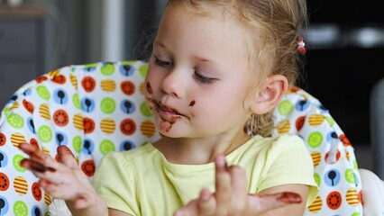 Wall Mural - Little girl with blond hair eating homemade chocolate with dirty mouth and hands in home kitchen