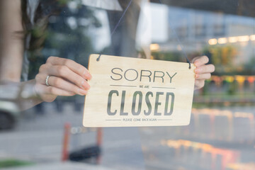 Female store owner turning close sign board of start up coffee shop cafe and restaurant through the door glass and closing the daily service