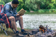 © puhimec - Close-up of bonfire with man reading a book in the background in nature.