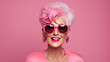© irissca - Senior fashion and trends. Stylish modern fashionable trendy senior older woman with short pink hair wearing pink cloth on pink background, fashion doll banner