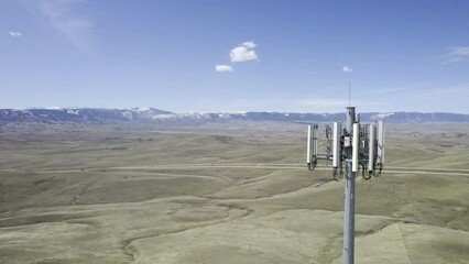 Cinematic drone shot flying backwards to reveal the 4G/5G antenna array at the top of a cell phone tower mast over a rural landscape (Aerial 4K HDR ProRes)