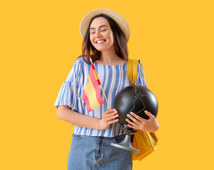 Wall Mural - Young woman with flag of Spain, globe and backpack on yellow background