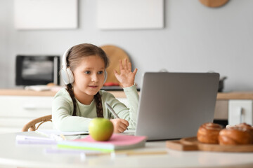 little girl in headphones with laptop studying computer sciences online at home