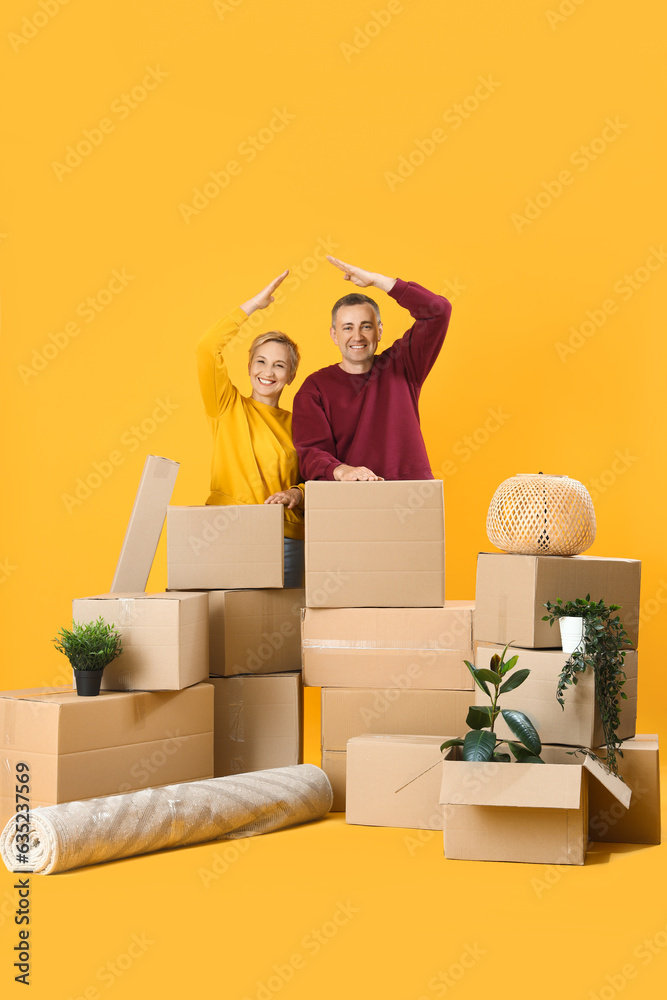 Mature couple with moving boxes on yellow background