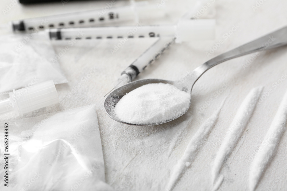 Spoon with drugs and syringes on light background, closeup