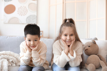 Poster - Cute little children in knitted sweaters sitting on sofa at home