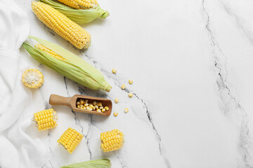 Fresh corn cobs and wooden scoop with kernels on white marble table