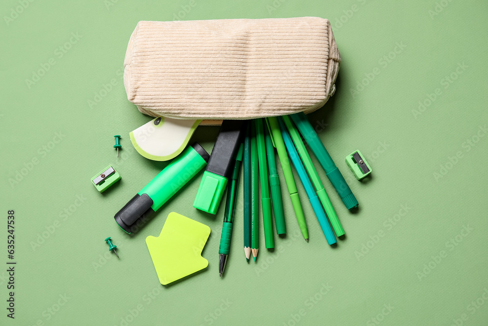 Pencil case with different school stationery on green background