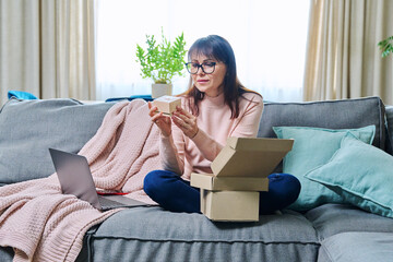 Mature woman sitting at home unpacking cardboard box with online shopping