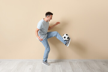 Sticker - Handsome man playing with soccer ball near beige wall