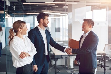 Wall Mural - Welcome to our team, mature modern men in formal wear shaking hands in modern office.
