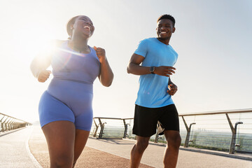 Authentic portrait of smiling African American man and woman running together outdoors. Happy plus size model training with personal trainer outdoors. Sport, motivation, healthy lifestyle concept 