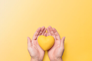 hands holding a yellow resin heart against a matching yellow background, symbolizing mental health a
