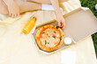 © Daryna  - A young man sits on a yellow mat and eats Neapolitan pizza from a box and orange juice in the middle of a park. The concept of recreation in nature, consumption of fast food and snacks, fast delivery