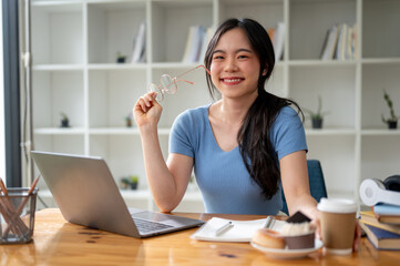 Wall Mural - A happy Asian female college student sits at her study table at home.