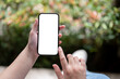© bongkarn - A female holding a smartphone mockup over a blurred outdoor garden in the background.