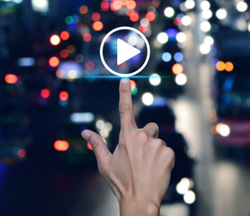 Sticker - Hand pressing play button flat icon over blur colourful night traffic jam road in city, Business music online concept