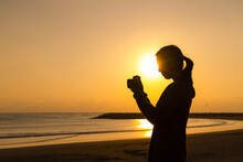 Silhouette Of Woman Use Camera To Take Photo At Sunset In The Beach
