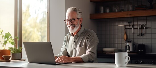 Elderly man in kitchen using laptop working online or browsing internet