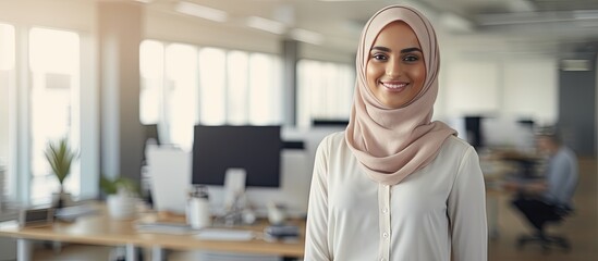 Confident young Muslim woman in modern office wearing a headscarf smiling at the camera waist up