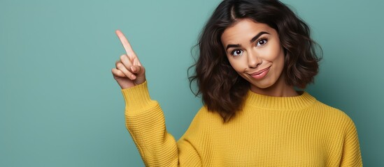 Wall Mural - Attractive young woman happily pointing upwards with a smile indicating empty space