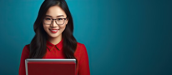 Poster - Chubby Asian girl wearing a red shirt in an office holding a tablet smiling in front of a blue background