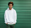 Photo of African-American teenager wearing a blank white hoodie standing in front of green wall, apparel mock-up, young man in sweatshirt