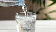 © Uuganbayar - Pouring soda water from bottle into glass on white wooden table, closeup