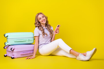 Poster - Full size photo of optimistic nice woman dressed purple t-shirt sit near baggage hold smartphone isolated on yellow color background