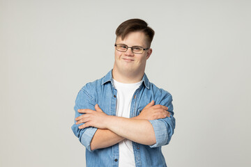 A smiling young man with cerebral palsy in glasses, jeans and a white T-shirt poses for the camera. World Genetic Diseases Day concept