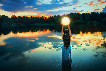 Art photo magic Fantasy woman and moon, holding universe planet in hands raises to dark night sky. Mystic witch Girl fairy elf river nymph stands in water lake summer nature. Lady queen back rear view