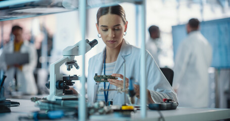 Aufkleber - Diverse Young Group of Engineers Working in a Startup Lab. Female Specialist Checking on Electronic Circuit Using Microscope While Project Managers Discuss Manufacturing Using Laptop Computer