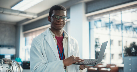 Poster - Portrait of Black Young Male Scientist Using Laptop Computer, Looking at Camera and Smiling in a Laboratory. Professional African American Man Working as Engineer, Monitoring Technology Projects