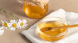 Chamomile syrup in a small bowl and in a jar and chamomile flowers on a linen kitchen towel