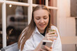 © zvkate - Beautiful happy girl in wireless earphones drinking water with lemon and mint while using mobile phone outdoor cafe.
