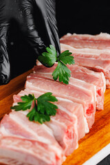 Wall Mural - Butcher woman hold fresh green and raw meat pork ribs with on wooden board on dark background