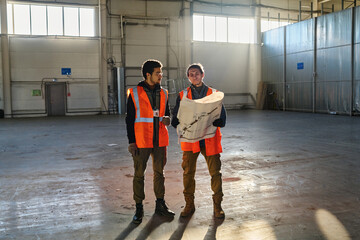 Leinwandbilder - Two young multiethnic consulting about details of building plan at meeting while one of them looking seriously at sketch on blueprint