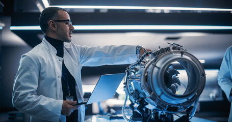 Wall Mural - Young Group of Engineers Collaborate on a New Type of a Gas Turbine Engine. Male Project Leader Holding a Laptop Computer and Explaining the Innovative Technology in Scientific Technology Lab