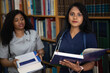 Two mixed race medical students in the library are preparing for an exam. Girl with a stethoscope and a book in her hands looks directly at the camera. Intern, doctor, preparation for treatment